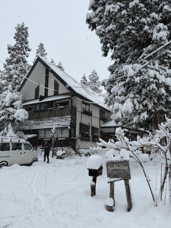 a snow covered house with a sign in front of it at Twin Peaks Lodge in Hakuba