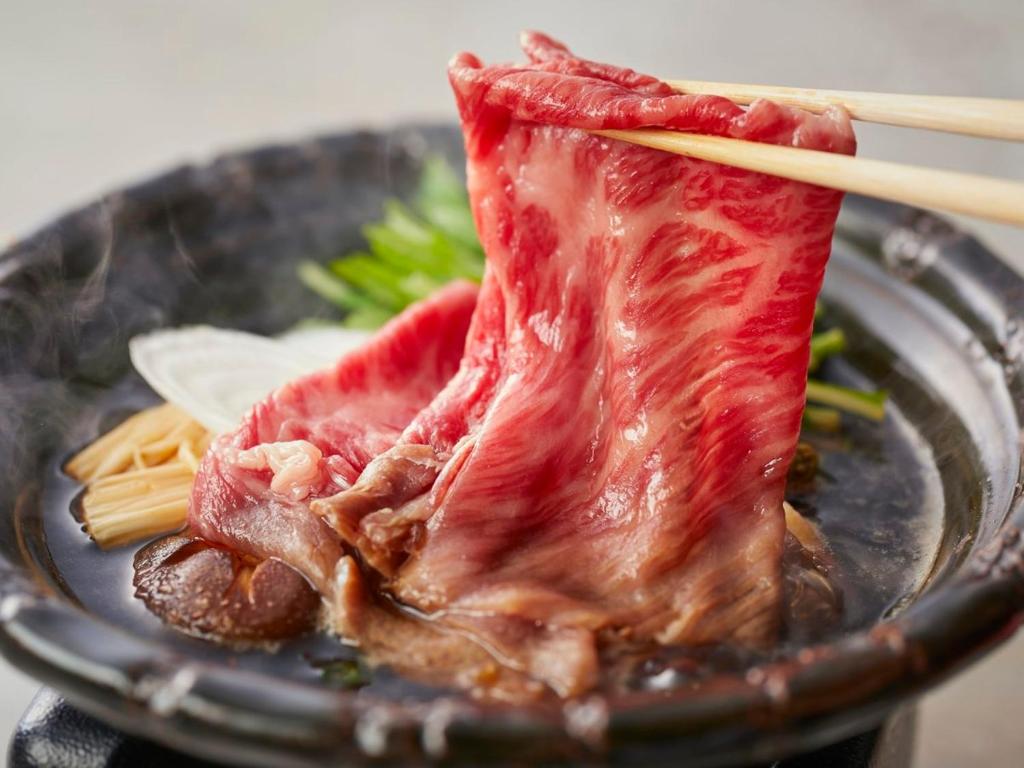 un morceau de viande dans un bol avec des pâtes et des baguettes dans l'établissement KAMENOI HOTEL Arima, à Kobe
