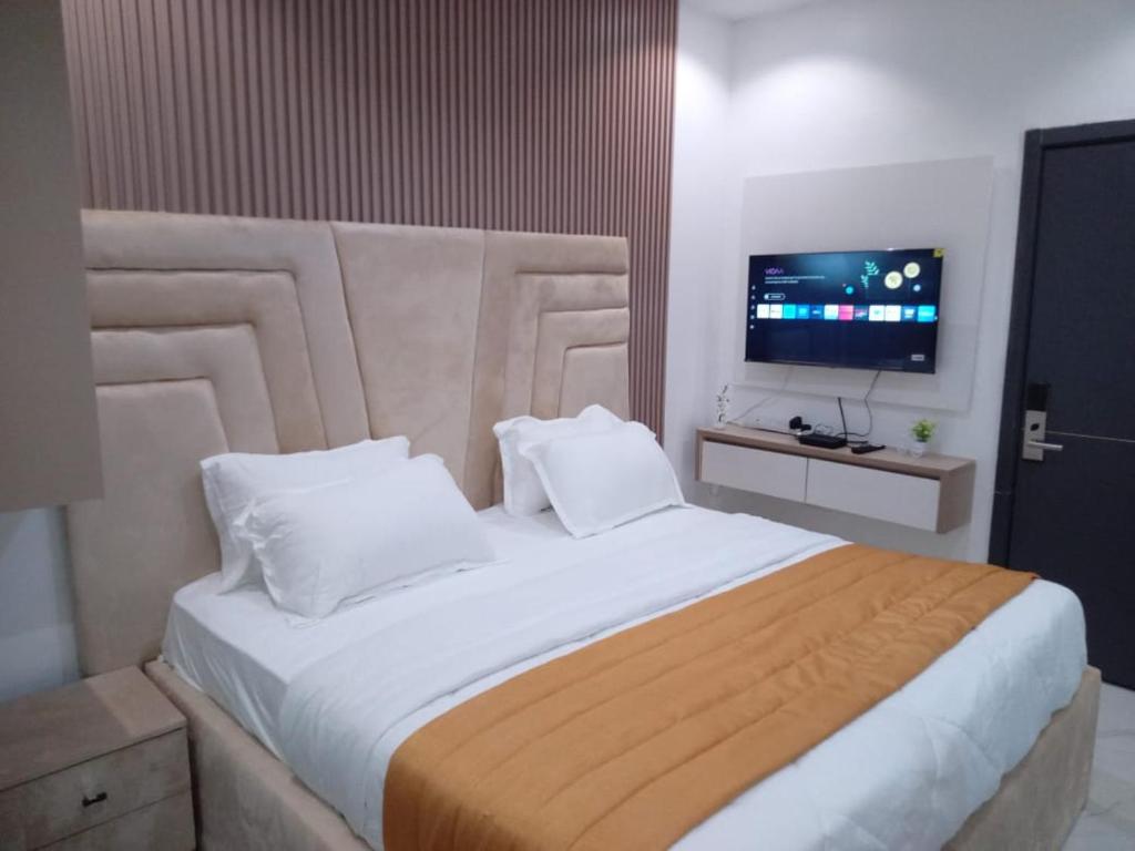 Agape Villa Luxury Apartments في بنين سيتي: غرفة نوم مع سرير أبيض كبير مع تلفزيون بشاشة مسطحة