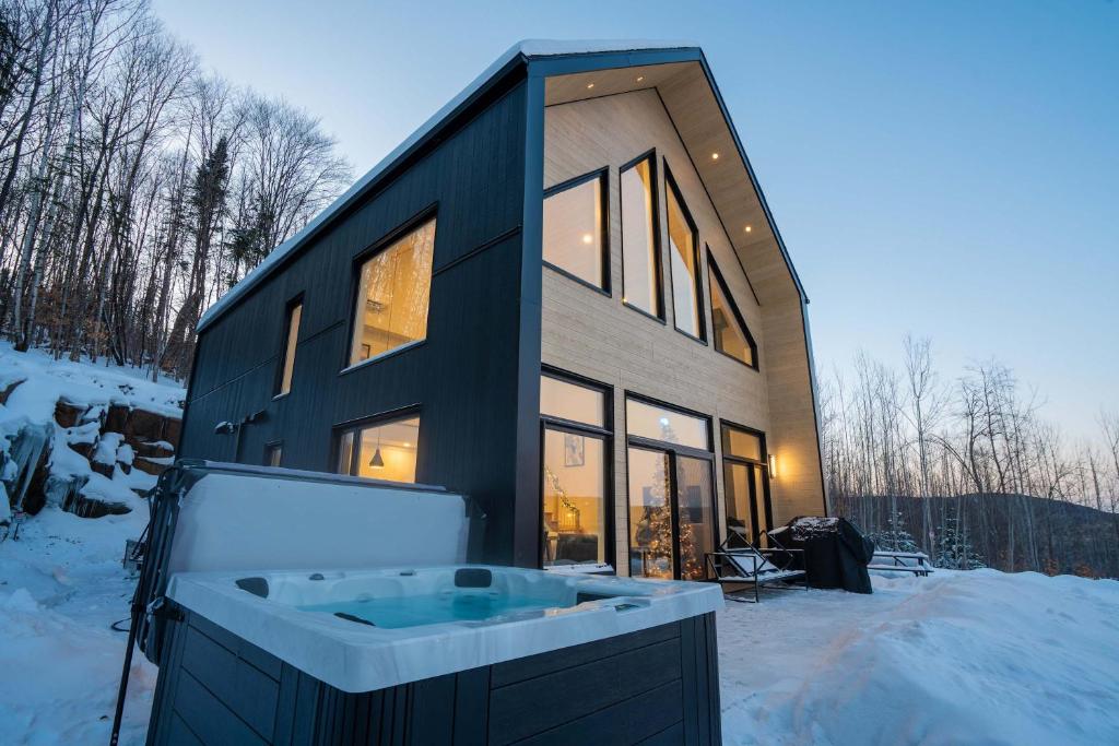 a black house with a tub in the snow at Chalet Le Valkea - Spa & Mountain in Saint Come