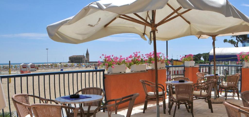 d'une terrasse avec des tables, des chaises et un parasol. dans l'établissement Hotel Giacomazzo, à Caorle