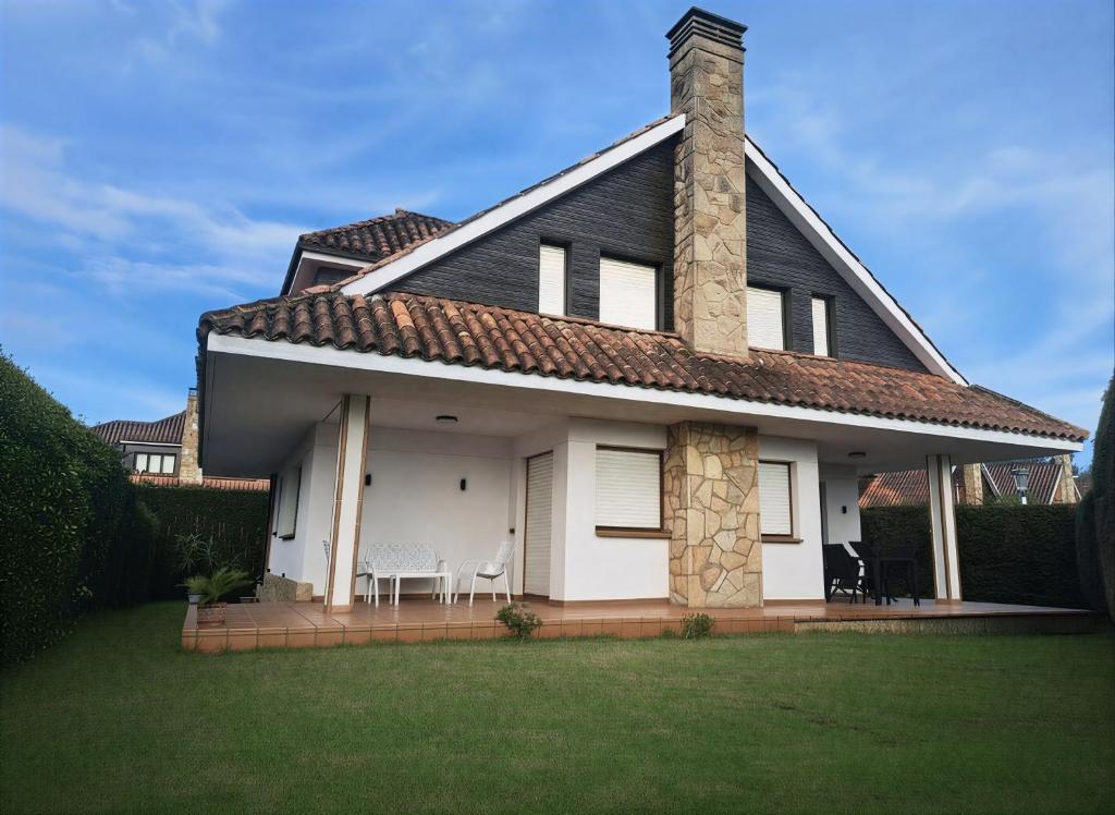 a white house with a chimney and chairs on a lawn at Casa Costera Gijón By Silastur in Gijón
