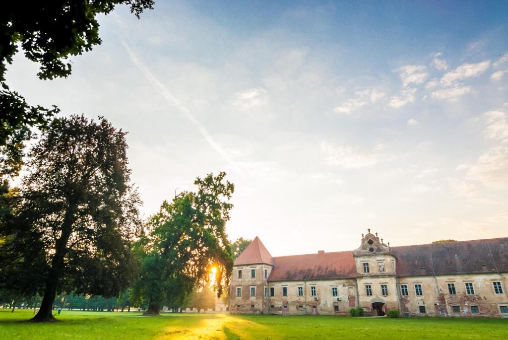 ein altes Gebäude mit einem Baum davor in der Unterkunft Dvorec Rakičan in Murska Sobota