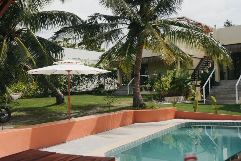 a swimming pool with an umbrella and palm trees at Casa De Amor Lambug in Badian