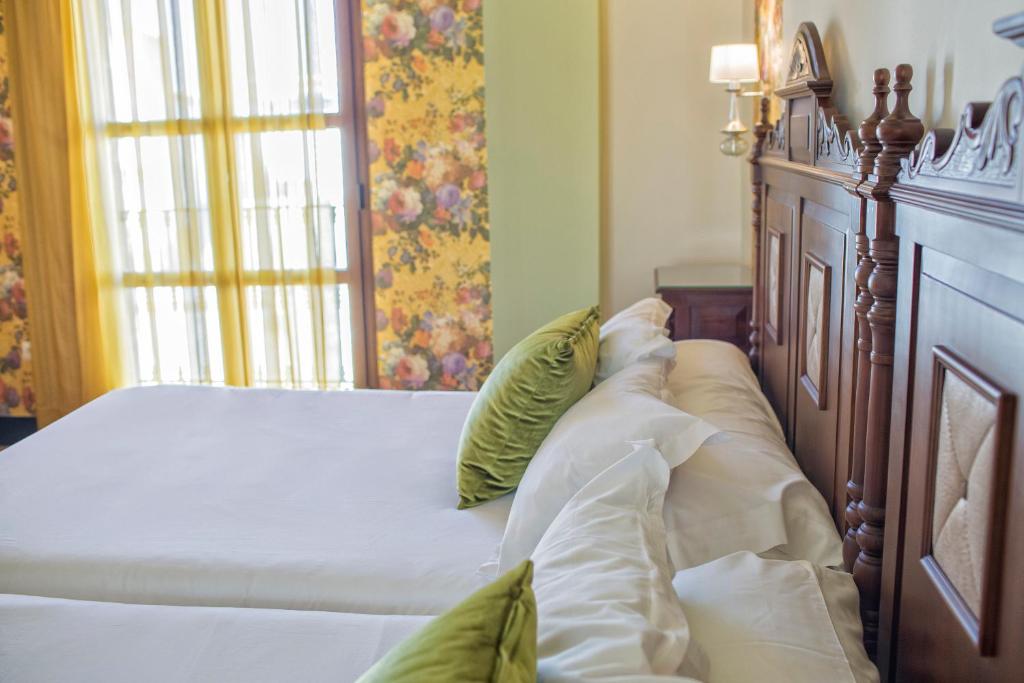 a bed with white sheets and green pillows at Hotel Rosaleda Don Pedro in Úbeda