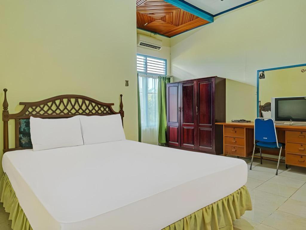 a bedroom with a bed and a desk and a television at Hotel O Tri Homestay in Palangkaraya