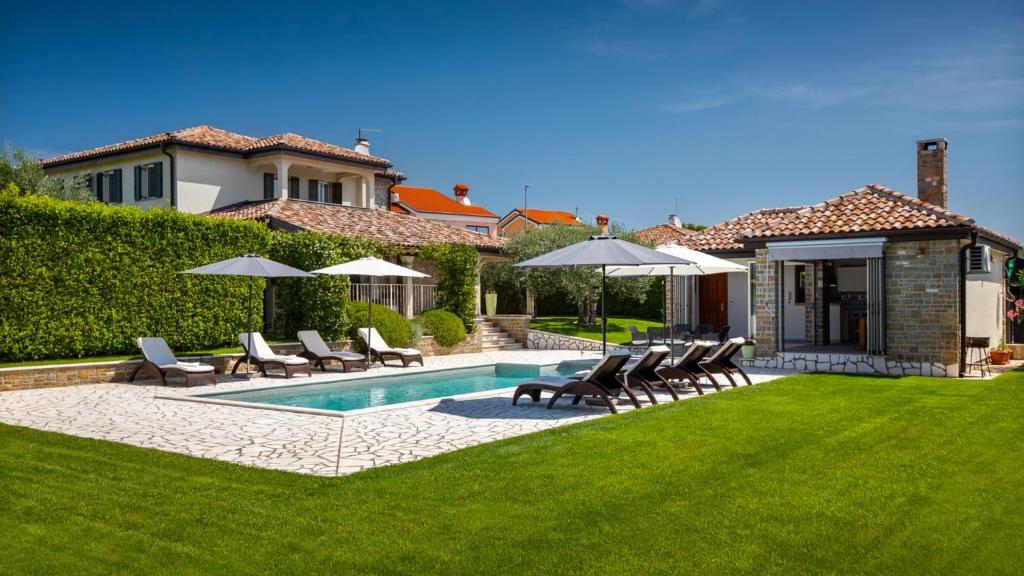 a backyard with a swimming pool with chairs and umbrellas at Rustic villa Inga with pool and grill in Buje in Kaštel