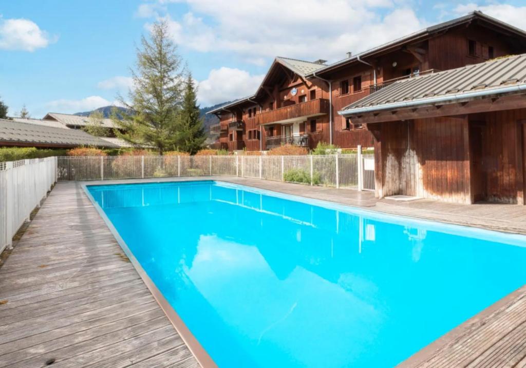 a swimming pool with a wooden deck next to a house at Chalet Triplex avec Piscine - Sauna in Samoëns