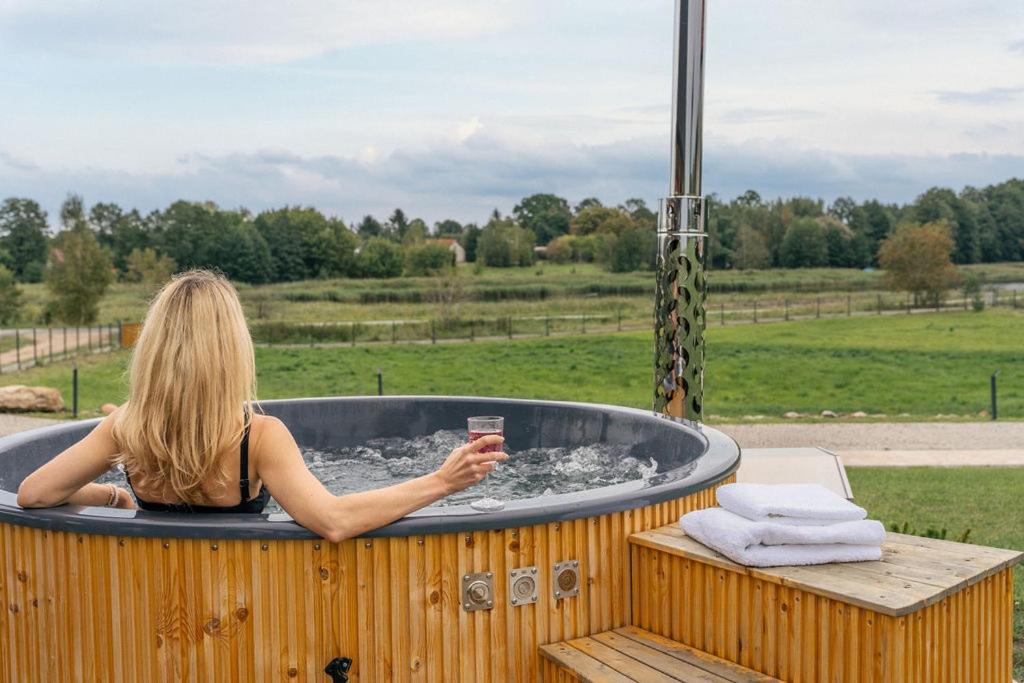 Rumiane pola - stodoła na Mazurach z widokiem na jezioro في Brajniki: امرأة تجلس في حوض استحمام ساخن مع مشروب