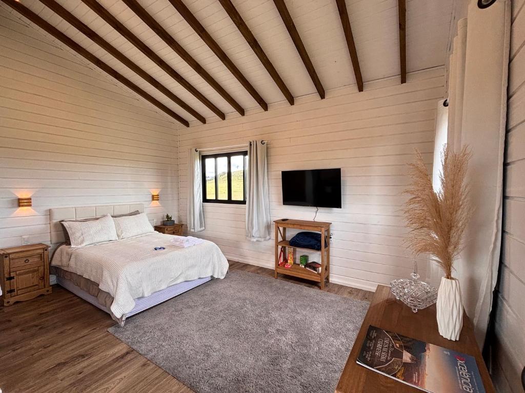 een slaapkamer met een bed en een flatscreen-tv bij Cabana Jardim das Nuvens in Urupema