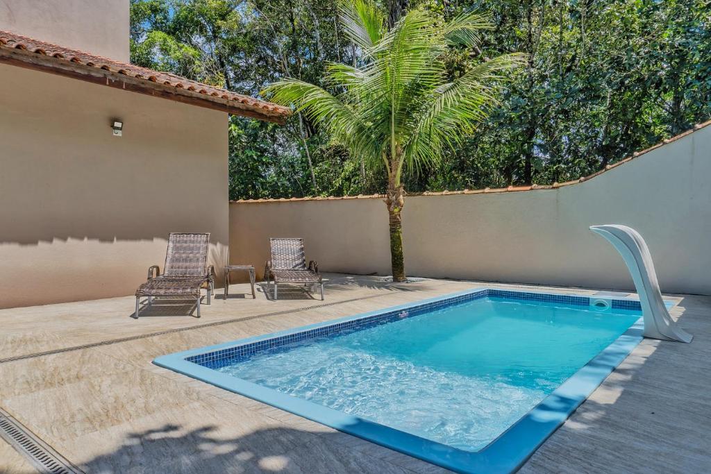 a swimming pool with two chairs and a palm tree at 400 m te Separam das Areias da Praia de Boraceia, casa com piscina aquecida para ate 12 pessoas in São Sebastião