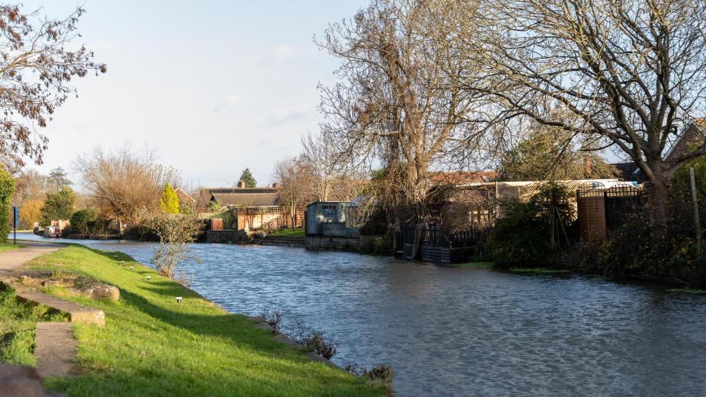 a river with trees and grass next to a house at Spacious Canalside Cottage - Games Room - Dog Walks in Loughborough
