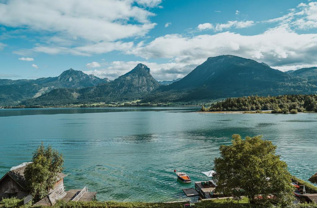 Un lago con dos barcos en el agua con montañas. en Strandhotel Margaretha, en St. Wolfgang