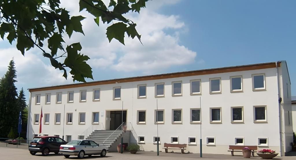 ein weißes Gebäude mit davor geparkten Autos in der Unterkunft Pension Clara in Tanneberg