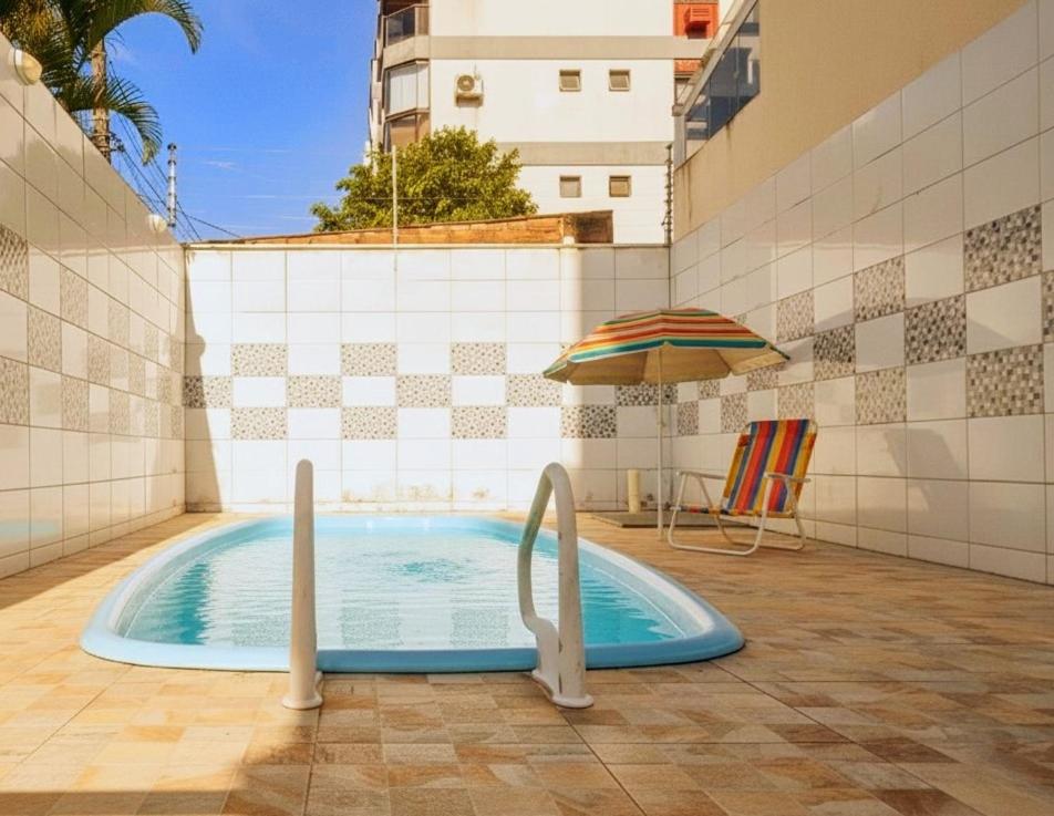 a swimming pool with an umbrella and a chair at Villa Enseada - Charme e conforto a 650m da Praia da Enseada in Guarujá
