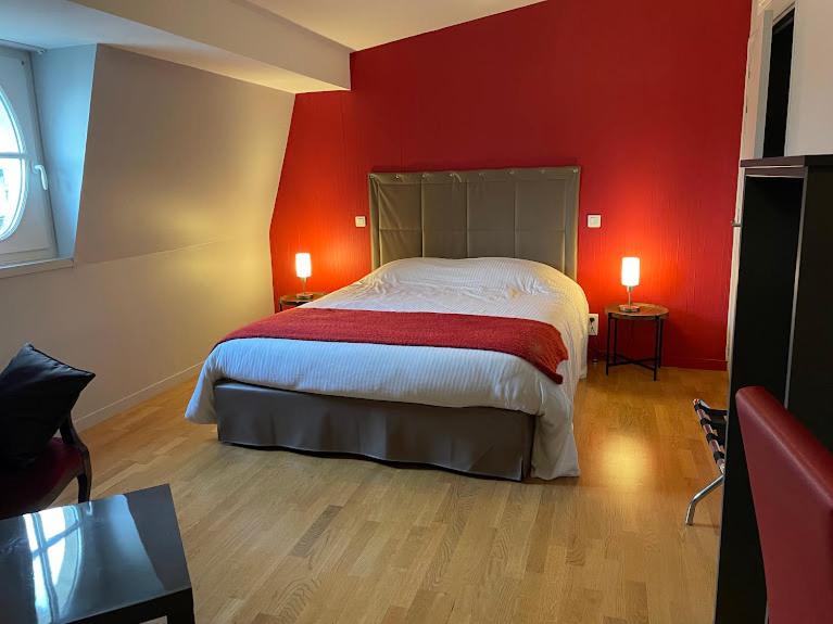 Hôtel Le Riche'Lieu في لوكون: غرفة نوم بجدار احمر فيها سرير ومصباحين