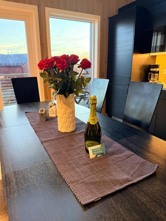 Una botella de vino sobre una mesa con un jarrón de rosas. en KB - Nordic Luxury Rorbu, en Stamsund