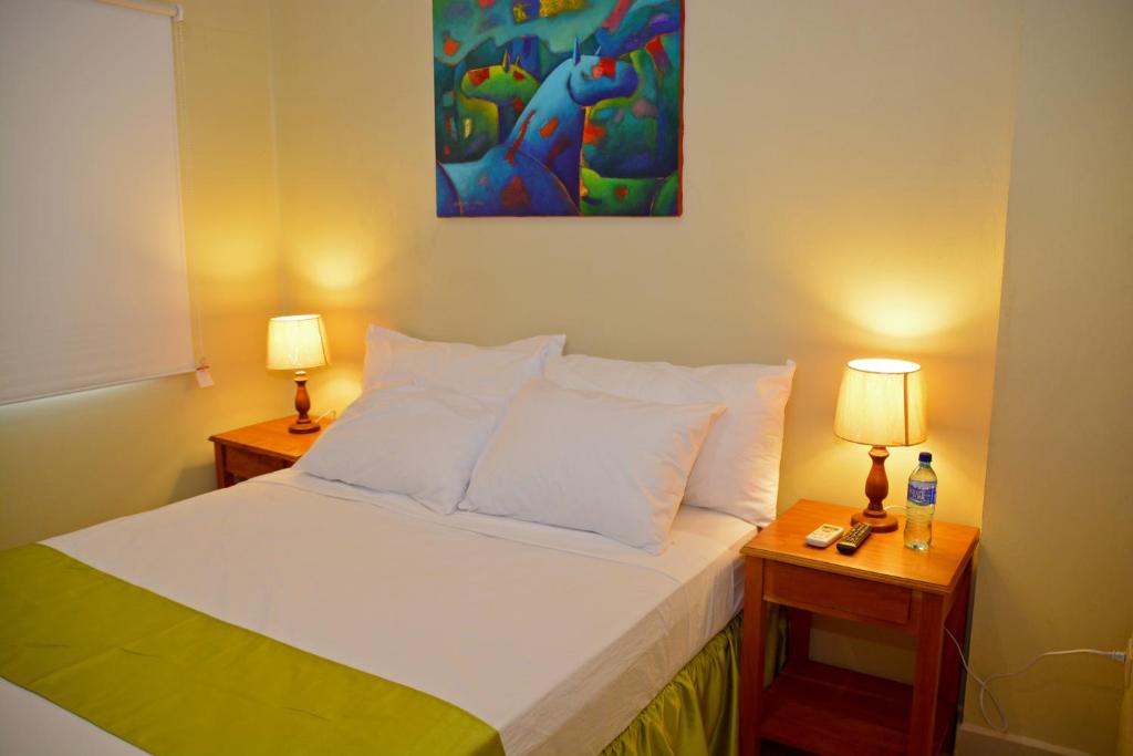 a bedroom with a bed with two lamps and a painting at Hotel Santa Martha in Managua