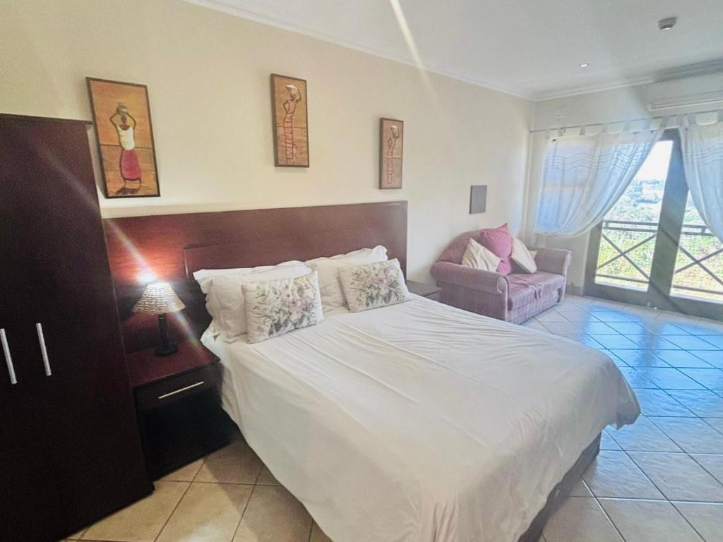 Un dormitorio con una gran cama blanca y una silla. en Ocean View Villas B09, en Port Edward