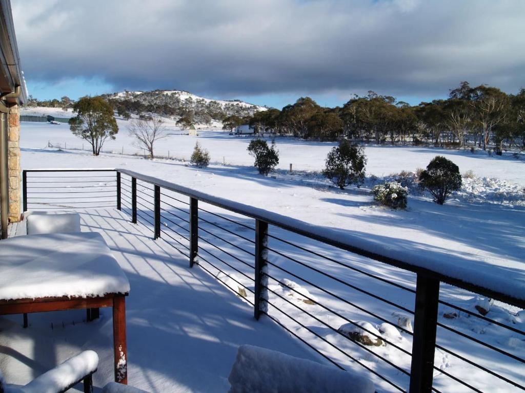 een met sneeuw bedekt balkon met een met sneeuw bedekt veld bij Runway View Cottage at Touchdown Cottages in Jindabyne