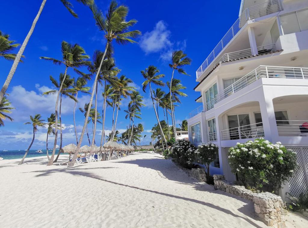 a white building on the beach with palm trees at Caribbean DELUXE VILLAS Los CORALES beach, POOL & SPA in Punta Cana