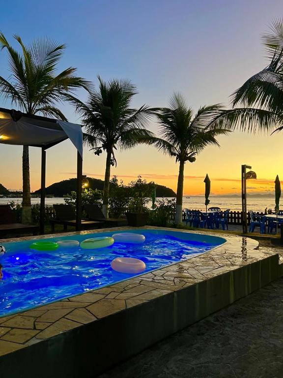 a large swimming pool with palm trees and the ocean at Pousada Coração da Ilha do Mel in Ilha do Mel