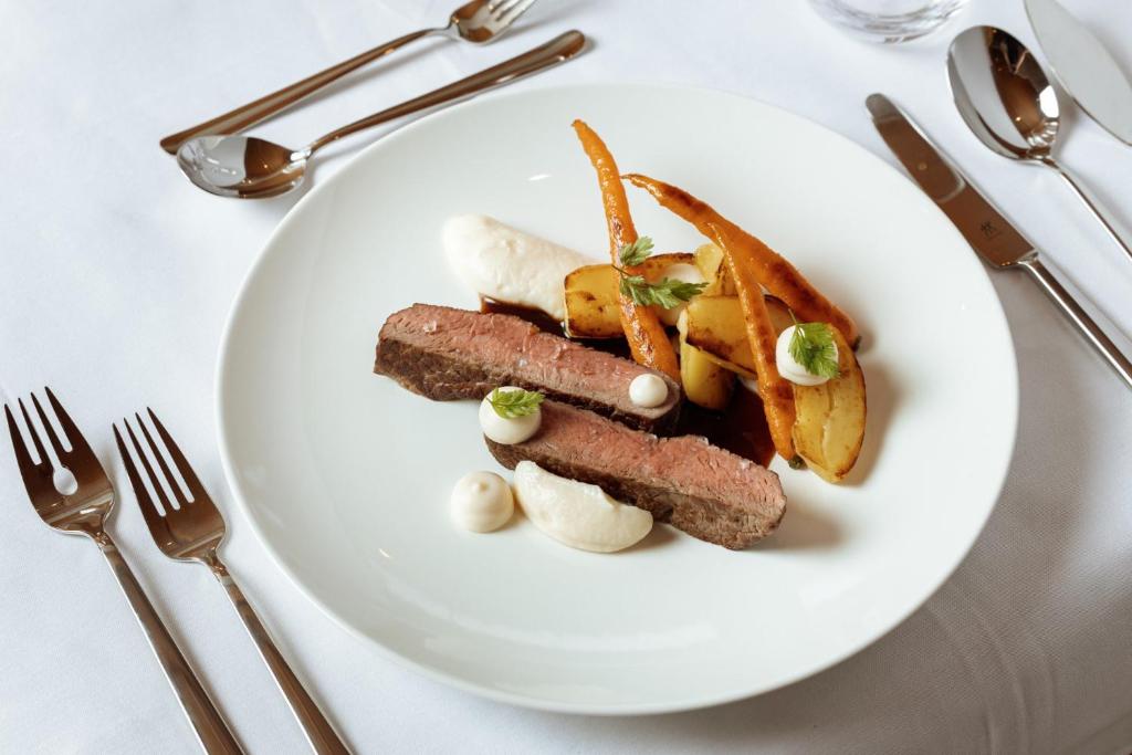 a white plate with meat and vegetables on a table at Apartment Hotel Elvis in Ortisei
