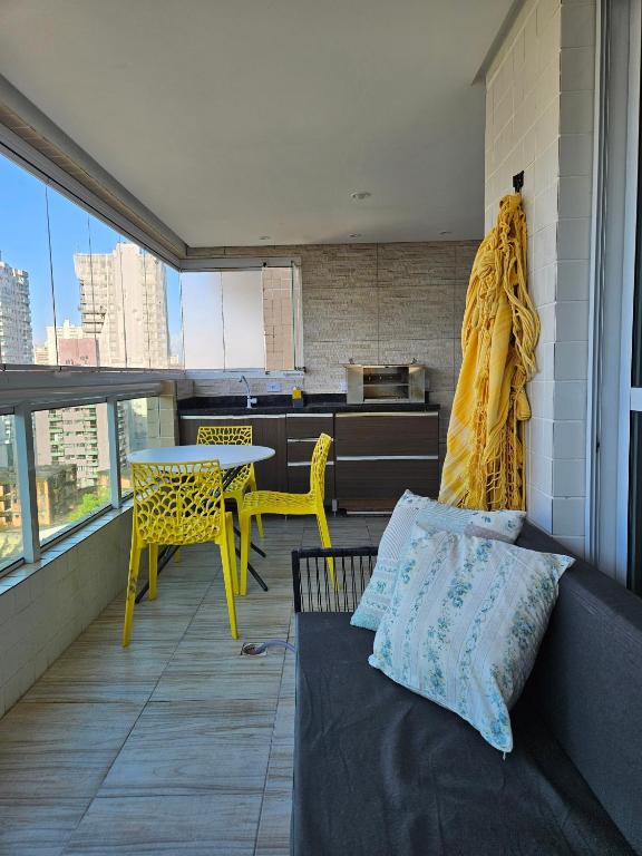 a balcony with a couch and a table and yellow chairs at Apto Novo no Canto do Forte PG in Praia Grande