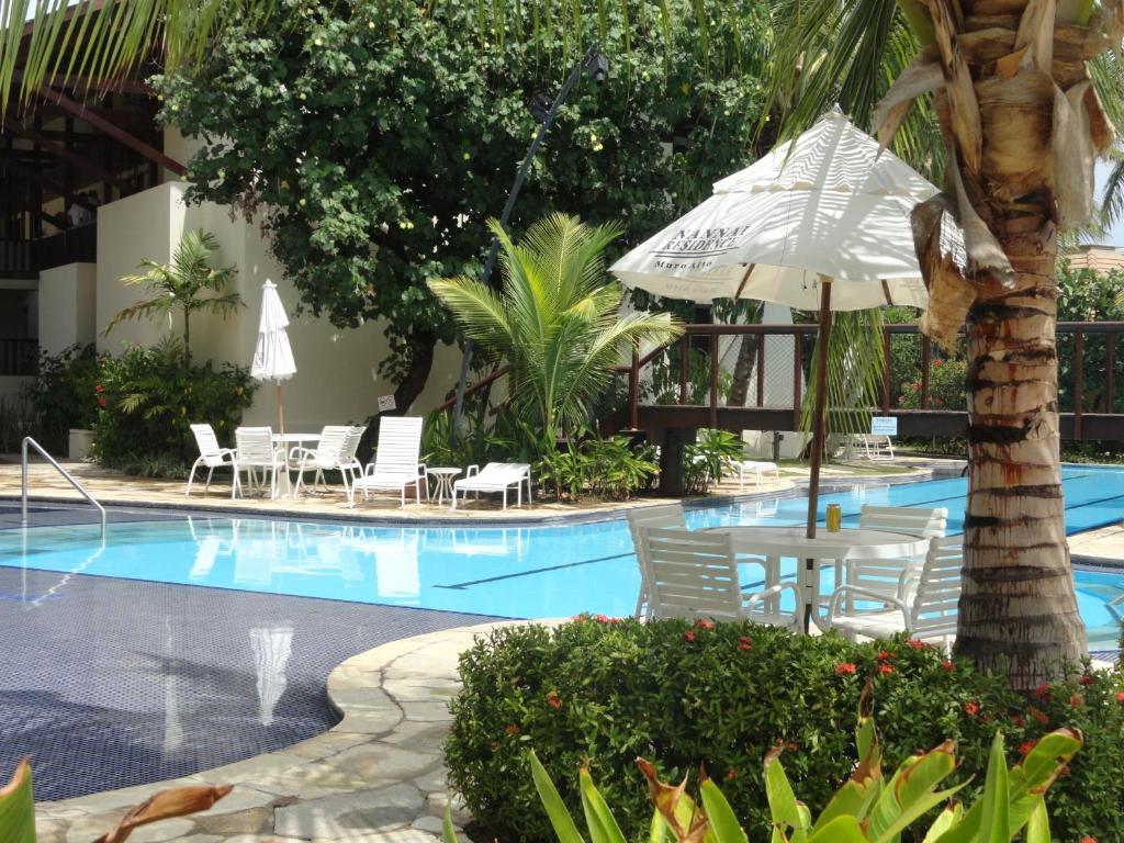 a swimming pool with chairs and an umbrella at Nannai residence Flat 202 in Porto De Galinhas