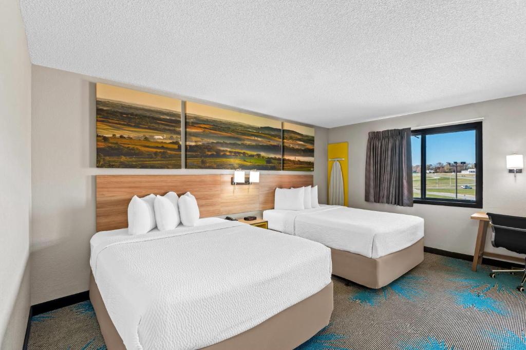 a hotel room with two beds and a desk at Days Inn & Suites by Wyndham Des Moines Airport in Des Moines