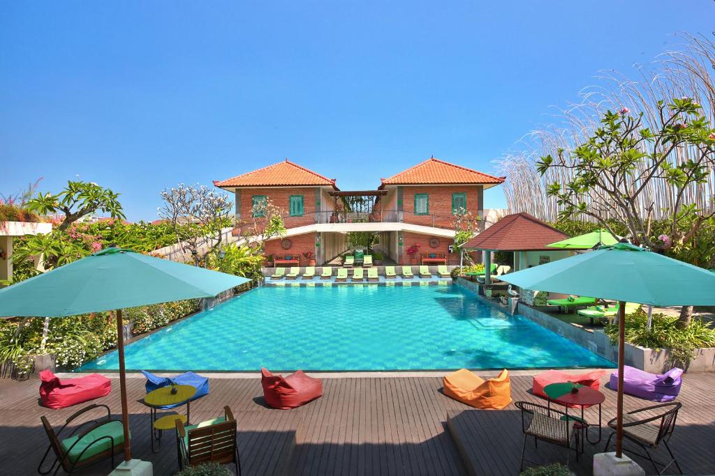 a pool with chairs and umbrellas in front of a house at Maison at C Boutique Hotel & Spa Seminyak in Seminyak