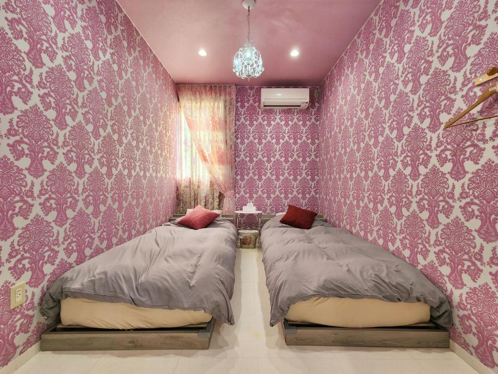 一棟貸しゲストハウス マリドール في إزومو: سريرين في غرفة نوم مع ورق جدران وردي