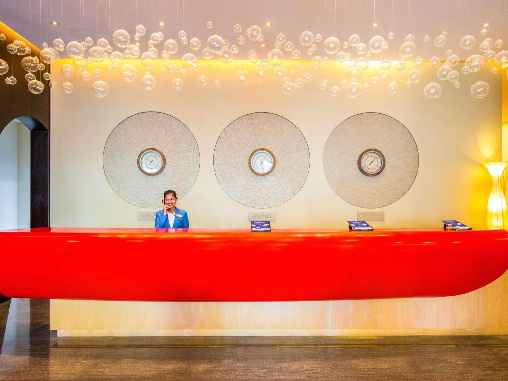 a man is standing behind a large red desk at ibis Mall Avenue Dubai in Dubai