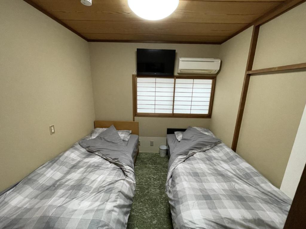two beds in a small room with a tv at 伊東駅前ゲストハウス in Ito