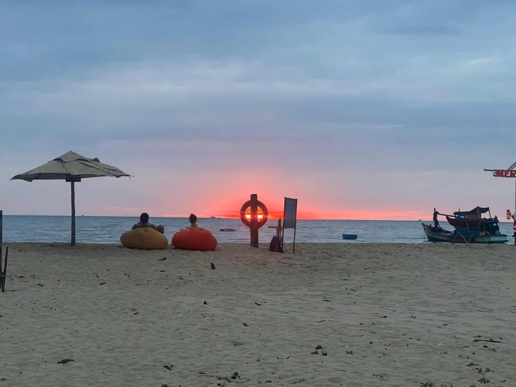 three people sitting on the beach watching the sunset at Bien Ngot Resort Phu Quoc in Phú Quốc