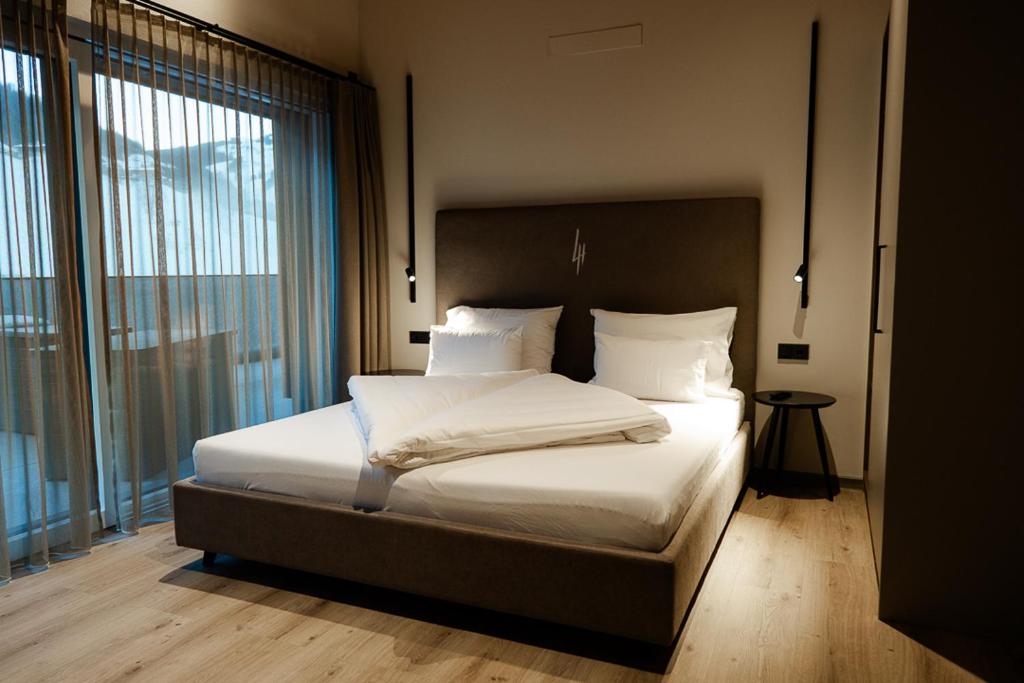 1 dormitorio con 1 cama con sábanas blancas y ventana grande en LH Suites Aparthotel - NEW since 2025, en Saalbach Hinterglemm