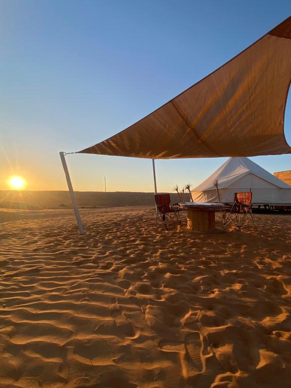 Een tent en stoelen op het strand bij zonsondergang. bij Sahara Dream Camp in Al Raka