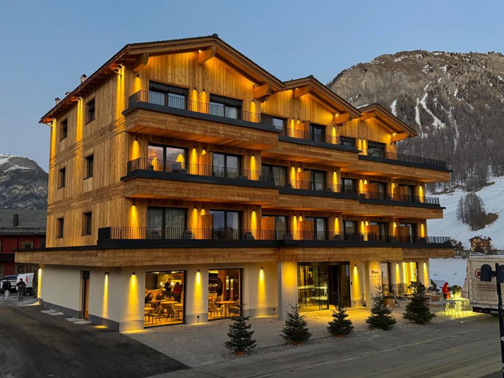 Un gran edificio de madera con una montaña al fondo. en Hotel Damelis, en Livigno