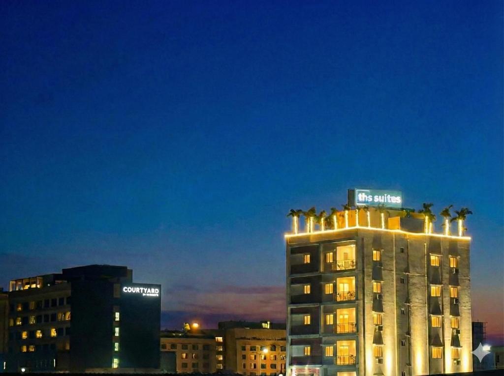 THS Suites - Luxurious 2 BHK AC apartments with Tirumala Views - Near Marriott, Taj and ITC 5 star hotels - Walkable to PS4, A2B, Orion, Starbucks cafes - Close to Thiruchanur and Alipiri flyover في تيروباتي: مبنى تعلوه أشجار النخيل ليلاً