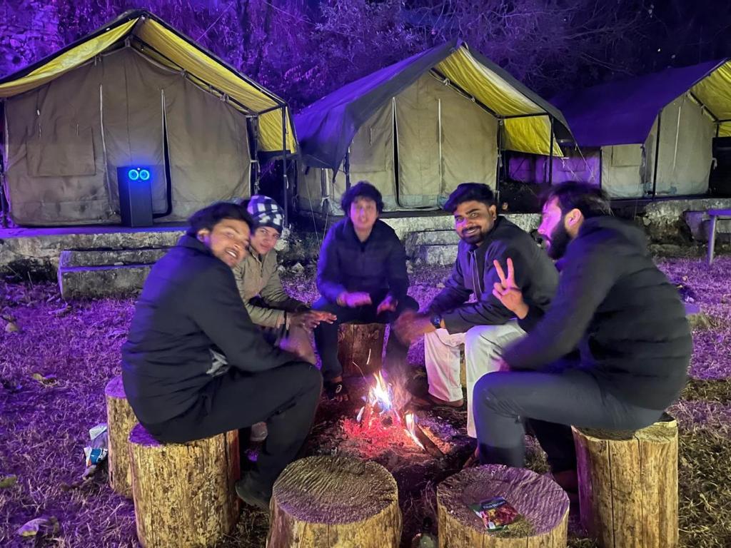 Un grupo de personas sentadas alrededor de un fuego frente a tiendas de campaña. en Royal Mount, en Kasol