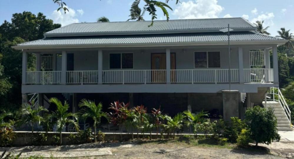 a white house with a porch and palm trees at La Retraite Apt in Rodney Bay Village