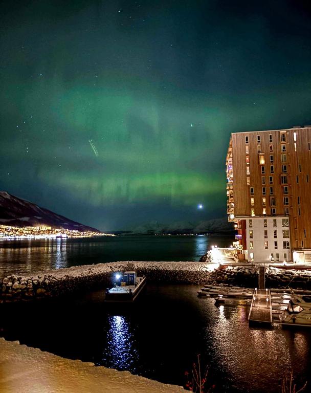 an aurora over a city with a boat in the water at New Aptartment Ocean View Central in Tromsø