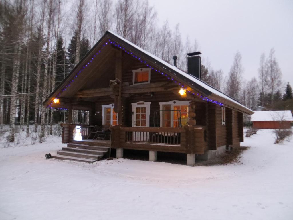 Una cabaña de troncos en la nieve con luces navideñas. en Cottage-karaoke Koivikko, en Äänekoski