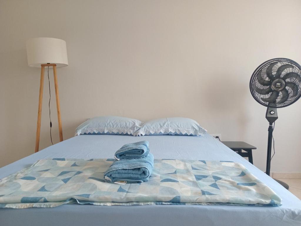 a bed with a blue blanket and a fan at Capsula Residence Hotel in Marília