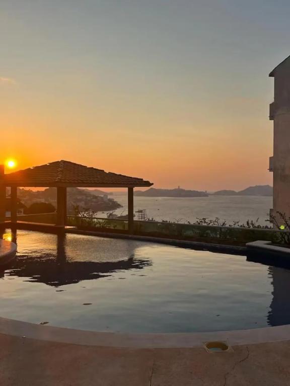 a sunset over a swimming pool with a gazebo at Casa las Palmas in Acapulco