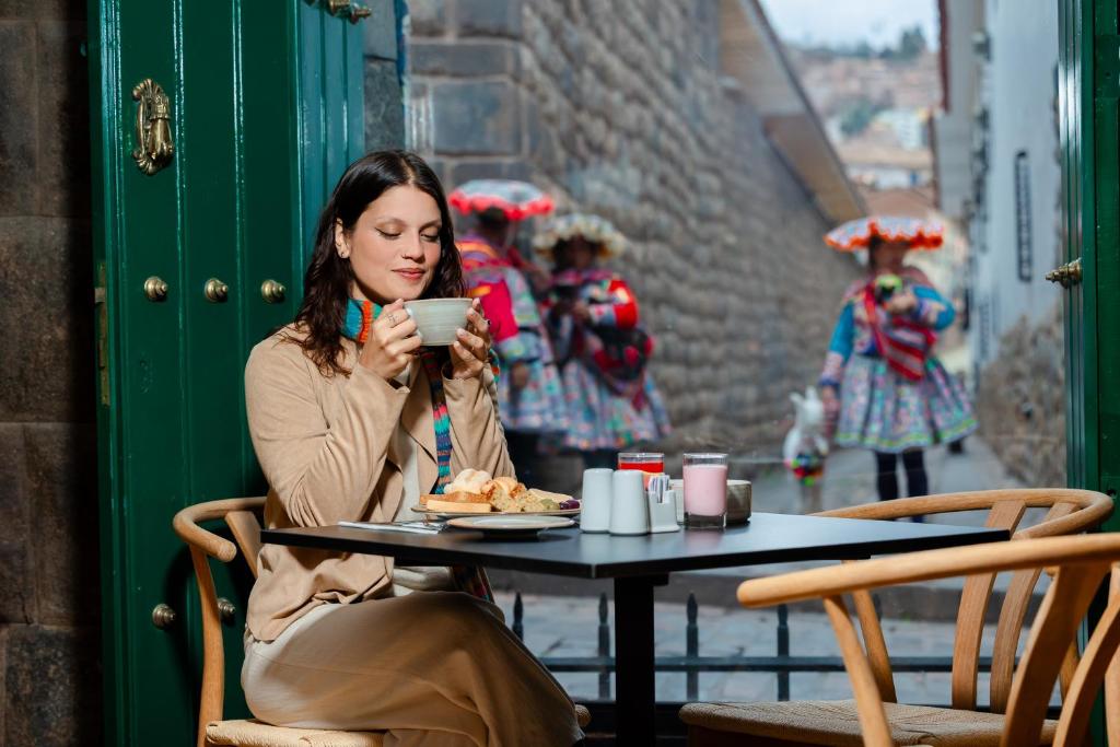 a woman sitting at a table with a cup of food at Hotel Hacienda Sonqori Centro Histórico in Cusco