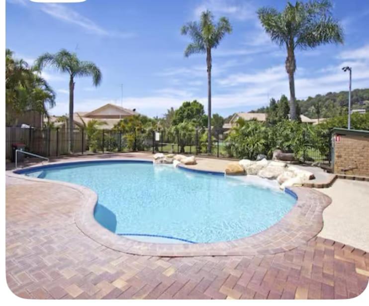 a large swimming pool in a yard with palm trees at Charming Townhouse Kirra Beach in Tweed Heads