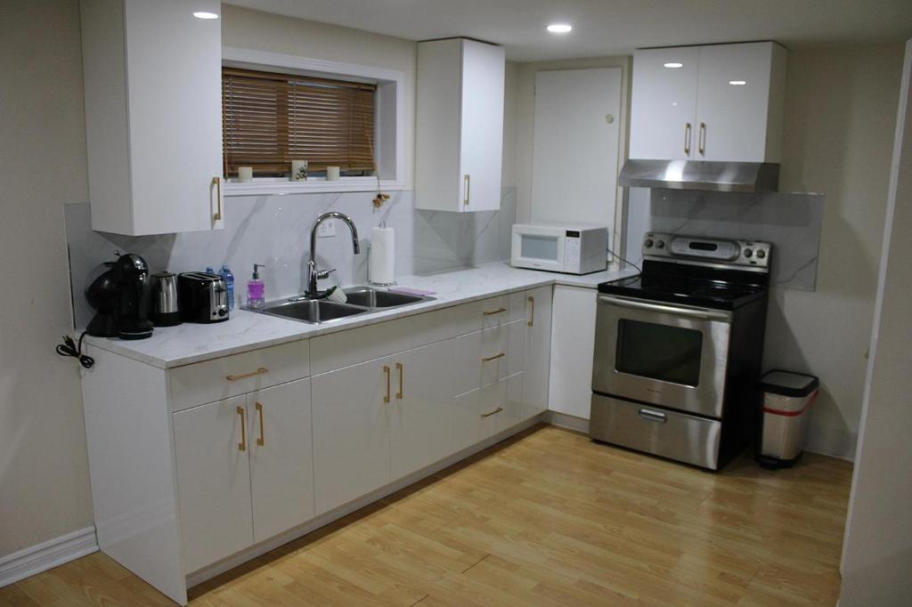 Una cocina con gabinetes blancos, un fregadero y una estufa. en Perfect location brand new basement 3 and half appartment, en Laval
