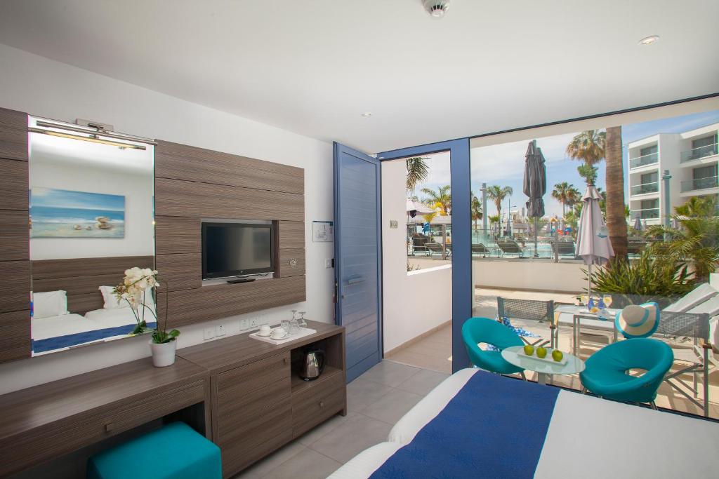 a bedroom with a bed and a tv and a balcony at Limanaki Beach Hotel & Suites in Ayia Napa