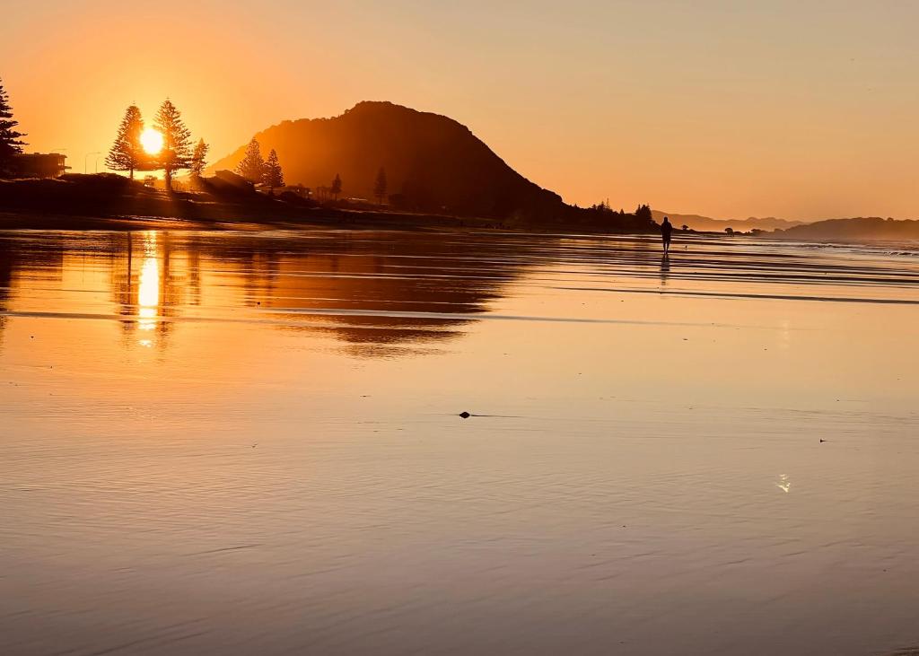 a sunset on a beach with a mountain in the background at Beachside Bliss in Tauranga